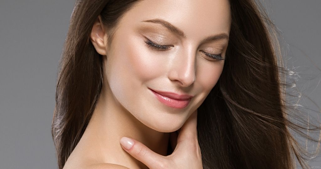 Woman with long dark hair looking downward with one hand resting near her neck (model).